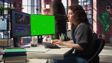 Kadın video yapımcısı, ajans ofisinde kroma anahtarının yanında bir multimedya projesini düzenleyerek, zaman çizgisi düzenleme ve video üretimini yönetmek için profesyonel teknoloji araçları ve kurgu yazılımı kullanır. Kamera A.