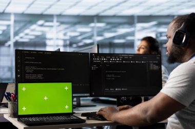Kulaklıkla müzik dinlerken sunucu çiftliğinde kodlanan adamın yanındaki izole ekran bilgisayarı. İşçi krom anahtar defteri ile yetkisiz erişime karşı donanımı koruyor, şarkılar duyuyor