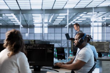 Veri merkezindeki Afrikalı Amerikalı adam sunucu mimarisinin konuşlandırılmasını koordine ediyor, veri işleme hızını artırıyor. Sunucu çiftliğinde müzik dinleyen işçiler, yapılandırma ve test ekipmanları