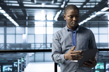 Veri merkezindeki bilgisayar bilimcisi rafların uyumunu doğrulamak için tablet kullanıyor. Kaynak kullanımını optimize eden, cihaz kullanılarak istikrarlı altyapıyı koruyan yüksek teknoloji tesisi uzmanı