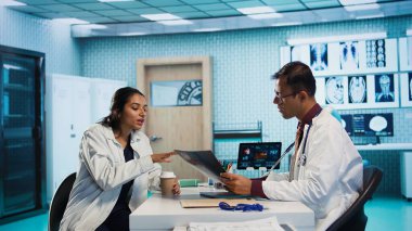 Uzman ve hasta modern bir muayenehanede teşhis sonuçlarını tartışıyor, röntgen görüntüleme sonuçları ve MRI taramaları sunmak için ileri teknoloji kuruluyor. Sağlık hizmetleri yönetimi. Kamera B.