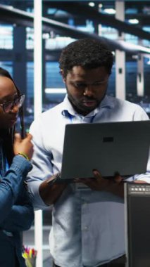 Verileri analiz etmek için düğüm ağacı yazılımı kullanarak sunucu tesisinde işbirliği yapan gülümseyen veri merkezi uzmanlarının dikey video portresi. Mutlu takım vitesi geliştirmek için görsel programlama kullanıyor