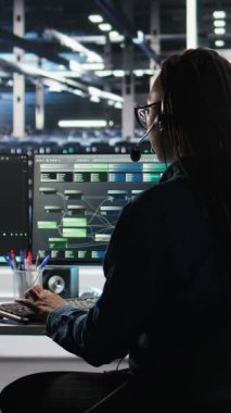 Dikey video veri merkezi uzmanı düğüm ağacı arayüzünü inceleyerek teknik destek sağlıyor. Sunucu odası teknisyeni iş arkadaşlarıyla mikrofonla konuşuyor, görsel programlama yazılımı kullanıyor, kamera A