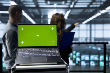 Bulanık arka planda sunucu odası teçhizatını denetleyen teknisyenlerin önünde izole edilmiş ekran maketi. Veri merkezi donanımlarını denetleyen yöneticilerin yanındaki krom anahtar defterini kapat