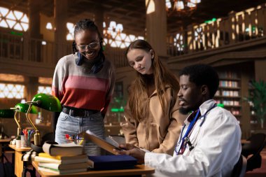 Bir kütüphanedeki çok ırklı öğrenci grubu, tıp kitapları ve materyalleri kullanarak farmakoloji ve mikrobiyoloji alanında uzmanlık kazanmak amacıyla doktorla birlikte bir derse katılıyor. Bilimsel çalışmalar için araştırma.