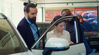 Araba galerisi satıcısı müşterilerden otomobil özelliklerini kontrol etmelerini ve mevcut modeller hakkında bilgi vermelerini istiyor. Ajan müşterilere araç kapısının dayanıklılığını gösteriyor, kamera A