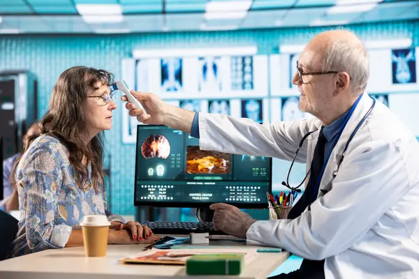 Yaşlı bir doktor, sağlık sorunları olan bir hastada dijital termometre kullanarak, kontrol sırasında ısıyı ölçerek bir kadına danışıyor. Sigorta ve sağlık sektörü danışmanlığında kıdemli müvekkil.