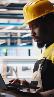 Güneş paneli fabrikasındaki dikey video mühendisi fotovoltaik sistem performansını dizüstü bilgisayardan inceliyor. Verimliliği ve sorun çıkarmayı optimize etmek için dizüstü bilgisayardaki üretim hattını analiz ediyorum. Kamera.