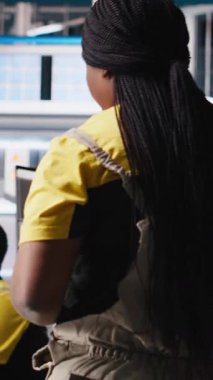 Dikey Video Siyah kadın teknisyen güneş paneli tasarımlarını endüstriyel yazılım üzerinde test ediyor, alternatif enerji üretim tesisinde çalışıyor. Üretim hattını optimize eden kadın mühendis. Kamera A.