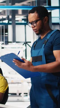 Dikey Video Photovoltaics fabrikası denetleyicisi, güneş santrali üretiminin endüstriyel yönergelerini gözden geçiriyor, robot kolları konveyör bantlarına güneş panelleri yerleştiriyor. Adam denetleme mekanizması parametrelerini okuyor