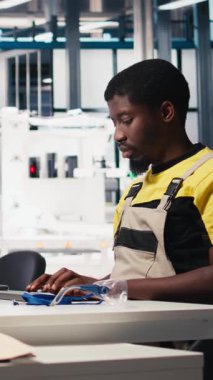 Dikey Video Siyah işçi güneş pili fabrikasındaki robot montaj hattını programlıyor. Otomasyon için yüksek teknoloji yazılımıyla çalışıyor. Erkek mühendis fotovoltaik sistemi ve makineleri test ediyor. Kamera B.
