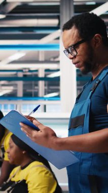 Fotovoltaik fabrikasındaki dikey video mühendisi, güneş panelleri montaj hatlarının performansını gözden geçirir, ince ayar için gerekli evrakları kontrol eder. Güneş pili makinelerini denetleyen denetçi. Kamera B.