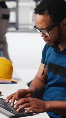 Fotovoltaik fabrikasındaki arızalı sistemleri araştıran dikey video mühendisi parametreleri bilgisayar ve tabletle karşılaştırıyor. Siyahi adam güneş panellerini inceliyor üretim tesisi, yüksek teknoloji. Kamera.