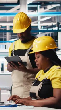 Fabrikadaki güneş paneli üretimi için bilgisayar, sorun çözme ve teknik sorunları çözme konusunda kalite kontrolü yapan dikey video Amerikan ekibi. İş arkadaşları sistemi inceliyor