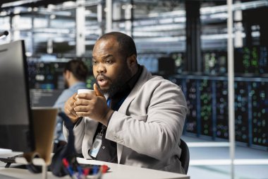 Veri merkezi teknisyeni kahve içiyor yazılım kayıtlarını analiz ediyor, depolama sistemlerini optimize ediyor. Sunucu odası çalışanı bilgisayardaki kaynak denetiminden keyif alıyor