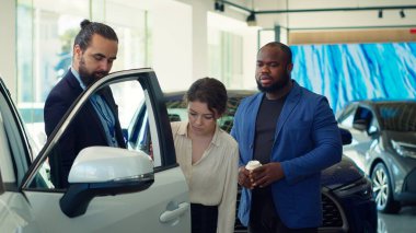 Araba satış temsilcisi müşterileri araç kapısına ve test kalitesine dokunmaya davet ederek bireylerin yatırım kararı almalarına yardımcı oluyor. Showroom temsilcisi müşterilerden otomobil özelliklerini, kamera A 'yı kontrol etmelerini istiyor.