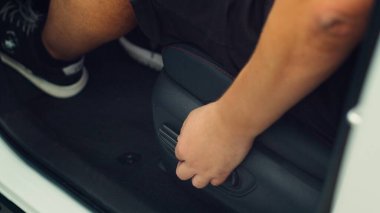 Arabanın içindeki adamın elektrikli düğmelerle ön koltuğu iterken yaklaş. Otomobil araç koltuğunun içindeki kişi ayarlama düğmelerini kullanarak direksiyona daha yakın.