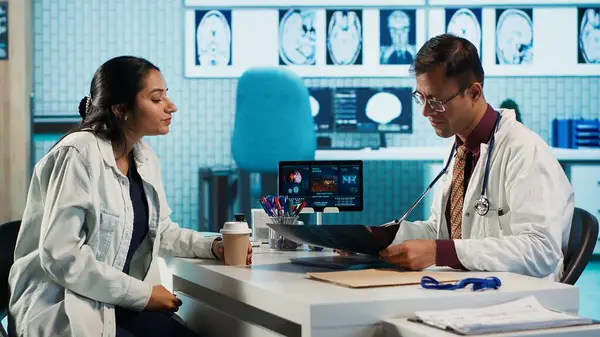Uzman ve hasta modern bir muayenehanede teşhis sonuçlarını tartışıyor, röntgen görüntüleme sonuçları ve MRI taramaları sunmak için ileri teknoloji kuruluyor. Sağlık hizmetleri yönetimi. Kamera A.