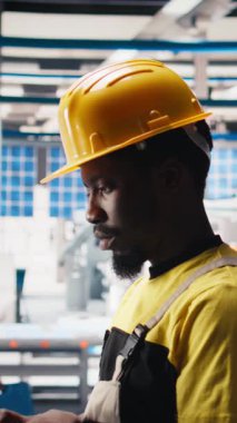 Dikey Video Photovoltaics fabrika teknisyeni dizüstü bilgisayar kullanarak üretim akışını optimize ediyor, şapka takıyor. Sürdürülebilir enerji güneş panelleri cihaz üzerindeki üretim sürecini izleyen bitki uzmanları