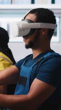 Güneş panellerindeki dikey video Afrikalı Amerikalı teknisyen VR gözlük kullanarak tesis kuruyor CAD yazılımı kullanarak yerleşimleri optimize ediyor. Fotovoltaik fabrika işçisi sanal gerçeklik teknolojisini kullanarak düzenlemeler yapıyor.