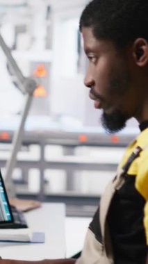 Dikey Video Siyah işçi güneş pili fabrikasındaki robot montaj hattını programlıyor. Otomasyon için yüksek teknoloji yazılımıyla çalışıyor. Erkek mühendis fotovoltaik sistemi ve makineleri test ediyor. Kamera A.