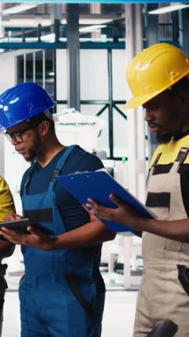 Güneş panelleri fabrikasındaki siyah çalışanlardan oluşan dikey video grubu cihazlar ve belgeler üzerindeki verileri inceliyor. Fotovoltaik tesisi mühendisleri yenilikçi güneş hücreleri dizayn prototipi üzerinde çalışıyorlar. Kamera.