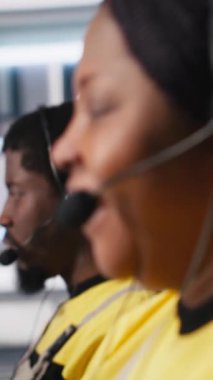 Vertical Video Customer, fotovoltaik tesisteki yardım masasında çalışan siyah mühendisi destekliyor. Kulaklıkla çağrılara cevap veriyor, teknik sorunları çözmede yardım ve destek öneriyor. Kadın operatör yardım alıyor