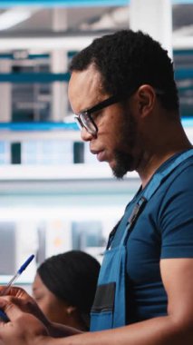 Dikey Video Photovoltaics fabrikası denetleyicisi, güneş santrali üretiminin endüstriyel yönergelerini gözden geçiriyor, robot kolları konveyör bantlarına güneş panelleri yerleştiriyor. Adam denetleme mekanizması parametrelerini okuyor