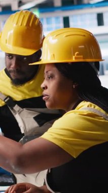 Dikey Afrikalı Amerikalı işçiler güneş paneli fabrikasındaki imalat ekipmanlarını kontrol ediyor, belge dosyalarını okuyor. Endüstriyel tesisteki mühendislerden oluşan bir ekip üretimi denetliyor.