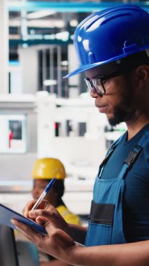 Dikey Video Siyah Fotovoltaik Fabrikası teknisyeni evrakları inceliyor, üretim verilerini analiz ediyor. Güneş panelleri sorun çıkarmak için dosya okuyan fabrika işçisi üretiyor