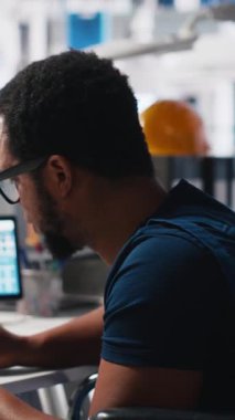 Dikey Video Afro-Amerikan tekerlekli sandalye kullanıcısı güneş enerjisi endüstrisinde çalışan fabrika mühendisi CAD yazılımını test ediyor. İşinde engelli bir uzman. Kamera A.