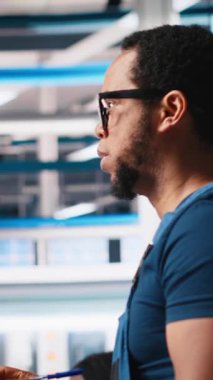 Fotovoltaik fabrikasındaki mühendisin dikey video portresi arızalı sistemleri tespit etmek için gerekli evrakları inceliyor. Güneş panelleri, dinlenme süresini azaltmak için inceleme dosyalarını okuyan fabrika işçisi. Kamera.