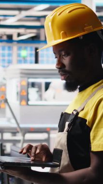 Güneş paneli tesisindeki dikey video teknisyeni fotovoltaik sistem performansını dizüstü bilgisayardan inceliyor. Endüstriyel santralde verimliliği optimize etmek için üretim çizgisi ölçümlerini analiz eden uzman