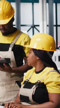 Fabrikadaki güneş paneli üretimi için bilgisayar, sorun çözme ve teknik sorunları çözme konusunda kalite kontrolü yapan dikey video Amerikan ekibi. İş arkadaşları sistemi inceliyor