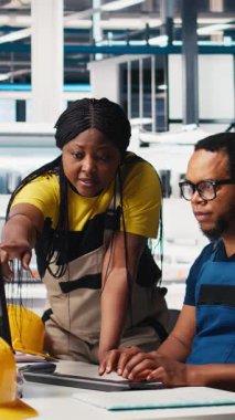 Dikey Video Photovoltaics fabrika ekibi güneş panelleri elle üretimini inceleyerek bilgisayar programındaki performansını izliyor. Siyahi çalışanlardan oluşan bir grup fabrika mekanizması parametrelerini okuyor. Kamera B.