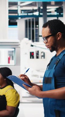 Güneş paneli fabrika incelemesinde dikey video müfettişi imalat ekipmanı ve üretim süreci, belge dosyalarını kontrol ediyor. Siyahi adam tesiste çevre dostu fotovoltaikleri sağlıyor. Kamera B