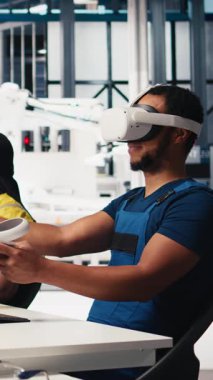 Dikey Video Photovoltaics fabrikası mühendisi VR kulaklıklı PC CAD yazılımı tasarlıyor, güneş panelleri imalat fabrikasında çalışıyor. Siyah uzman sanal gerçeklikteki montaj hatlarını inceliyor