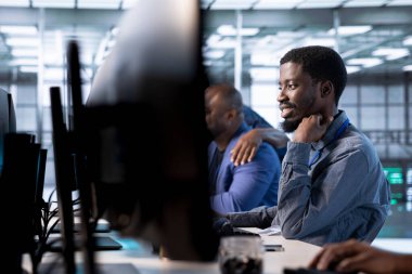 Veri merkezindeki gülümseyen mühendis, performansı arttırmak ve sunucuları yazılım zayıflıklarından korumak için sistemleri güncelliyor. İş arkadaşları sunucuların yavaşlamasına yol açan hatalar arıyor