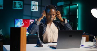 Teleworker şirket projesi için verileri araştırırken müziğin tadını çıkarıyor, bir gecede kişisel ev ofisinde görevler yapıyor. Dizüstü bilgisayarın önünde oturan ve kulaklık kullanan bir kadın, kamera B