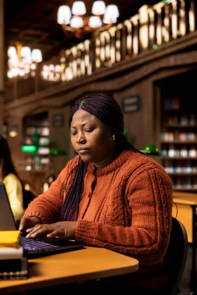 Afrikalı Amerikalı özel öğretmen bir okul kütüphanesinde ders için belgeler hazırlıyor ve öğrenme materyalleri hazırlıyor. Akademik kaynak sağlayan zeki profesör eğitim alanında danışmanlık yapıyor..