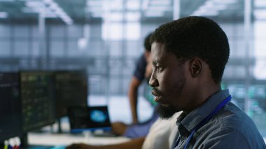 Sunucu merkezi çalışanlarına odaklanın felaket kurtarma planları geliştirerek en az dinlenme süresini sağlayın. Veri merkezinde performansı izlemek için veri analizi kullanan Afrikalı Amerikalı bir adam, kamera A