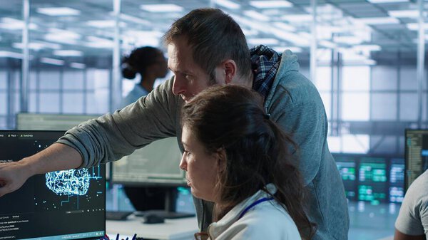 IT team members programming scripts on computer, employing AI machine learning. Software developer and coworker manipulating lines of code for artificial intelligence applications, camera A
