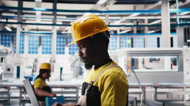 Fotovoltaik fabrikası teknisyeni dizüstü bilgisayar kullanarak üretim akışını optimize ediyor, şapka takıyor. Sürdürülebilir enerji güneş panelleri cihaz üzerindeki üretim sürecini izleyen bitki uzmanları. Kamera B.