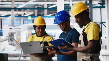 Güneş panelleri mühendisleri ekibi fabrikadaki cihazları kullanarak yeni fotovoltaik materyaller geliştiriyor. Siyahi işçi grubu daha iyi üretim bandı için deneyler yapıyor. Kamera A.