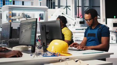 Çalışanlar, yüksek teknolojili sürdürülebilir bir tesiste güneş enerjisi fabrikasında robotik silahları kontrol etmek için bilgisayar kullanıyorlar. Teknisyen otomasyon ayarlarını tutarlı üretimi destekleyecek şekilde ayarlar. Kamera B.