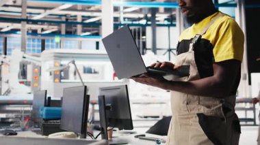 Fotovoltaik fabrikasındaki siyah mühendis arızalı sistemleri tespit etmek ve hata ayıklamak için dizüstü bilgisayar kullanıyor. Güneş panelleri üreten fabrika işçisi, çalışma süresini azaltıyor, sorun yaratıyor. Kamera B.