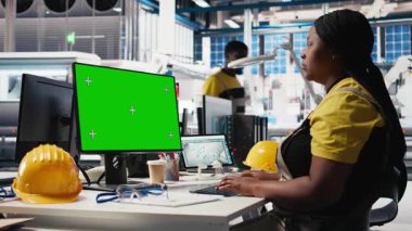 Fotovoltaik fabrikasındaki siyah teknisyen model bilgisayarda sistemi gözden geçirip hataları tespit etmek için programı inceliyor. Fotovoltaik fabrika işçisi üretim parametrelerini monitörde ayarlıyor. Kamera B.