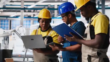 Fotovoltaik fabrikasındaki teknisyen grubu cihazlar üzerinde izleme yazılımı kullanıyor, sorunsuz üretim hattı için sorun yaratıyor. Siyah takım, güneş panelleri üreten robotları inceliyor. Kamera A.