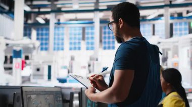 Güneş paneli fabrika teftişinde müfettiş üretim ekipmanları ve üretim süreci, belge dosyalarını kontrol ediyor. Siyahi adam tesiste çevre dostu fotovoltaikleri sağlıyor. Kamera A.