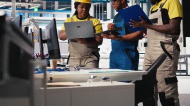 Fotovoltaik fabrikasındaki teknisyen grubu cihazlar üzerinde izleme yazılımı kullanıyor, sorunsuz üretim hattı için sorun yaratıyor. Siyah takım, güneş panelleri üreten robotları inceliyor. Kamera B.